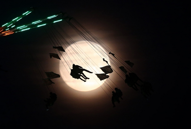 People on a funfair ride are silhouetted against the moon a day before the "supermoon" spectacle, in London, Britain November 13, 2016.    REUTERS/Neil Hall