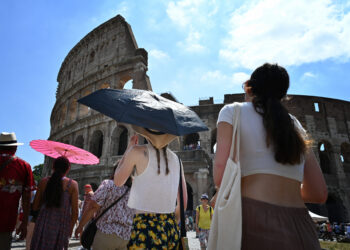 Tourists shelter from the sun with umbrellas near the Colosseum in Rome, on July 14, 2023, as Italy is hit by a heatwave. (Photo by Alberto PIZZOLI / AFP)