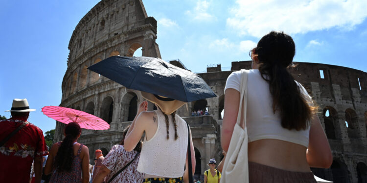 Tourists shelter from the sun with umbrellas near the Colosseum in Rome, on July 14, 2023, as Italy is hit by a heatwave. (Photo by Alberto PIZZOLI / AFP)