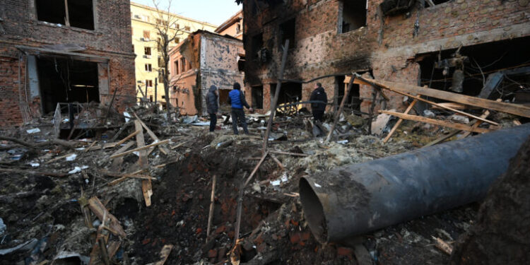 Local residents inspect damages outside an apartment building after the overnight Russian drones attack in Kharkiv, December 31, 2023, amid the Russian invasion of Ukraine. Kyiv said on December 31, 2023, it destroyed 21 of 49 Iranian-made "Shahed" drones fired by Russia overnight, adding that six guided missiles had also targeted the northeastern city of Kharkiv. (Photo by SERGEY BOBOK / AFP)