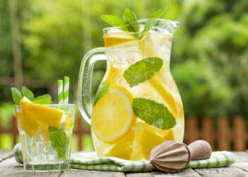 Lemonade pitcher with lemon, mint and ice on garden table