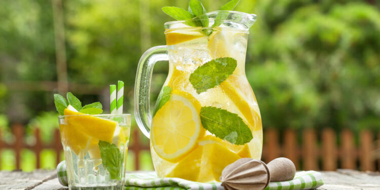 Lemonade pitcher with lemon, mint and ice on garden table